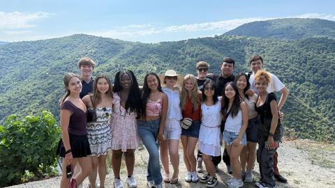 Group of students posing together outdoors with green hills and blue sky in the background.