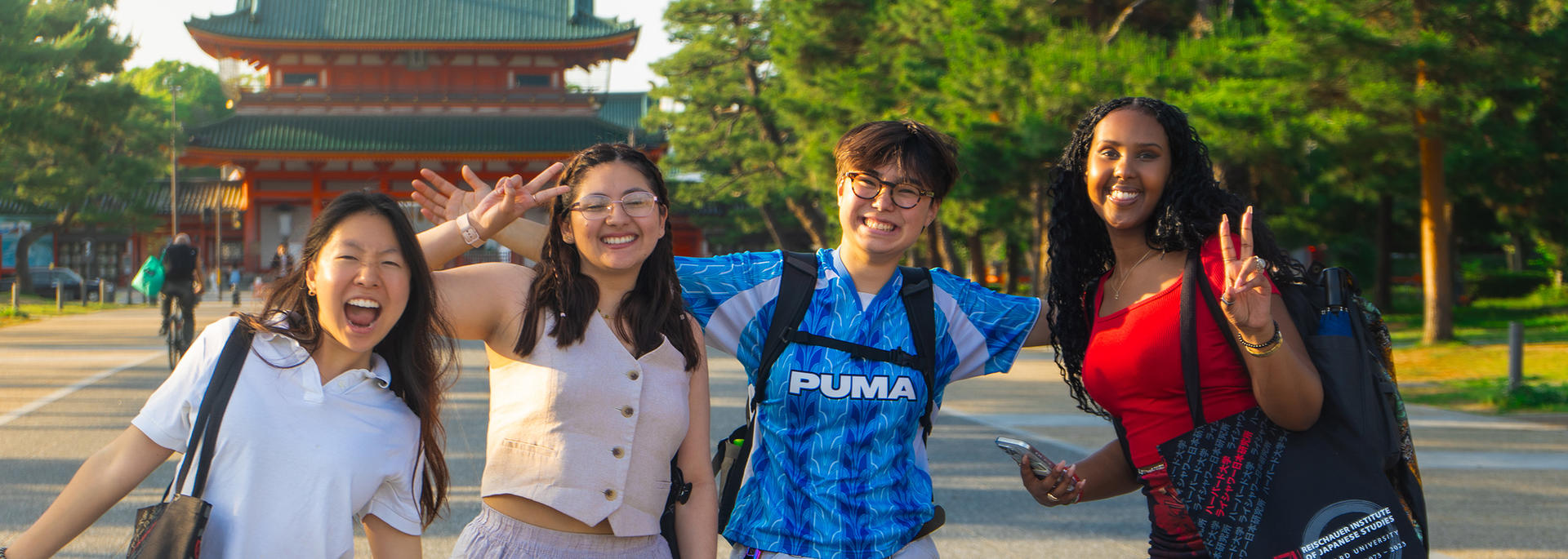 Four smiling students pose and make peace signs in front of a traditional Japanese gate.
